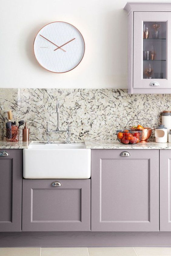 una moderna cucina grigio lilla con ripiani in pietra e alzatina, con un orologio bianco e un lavandino sembra molto chic