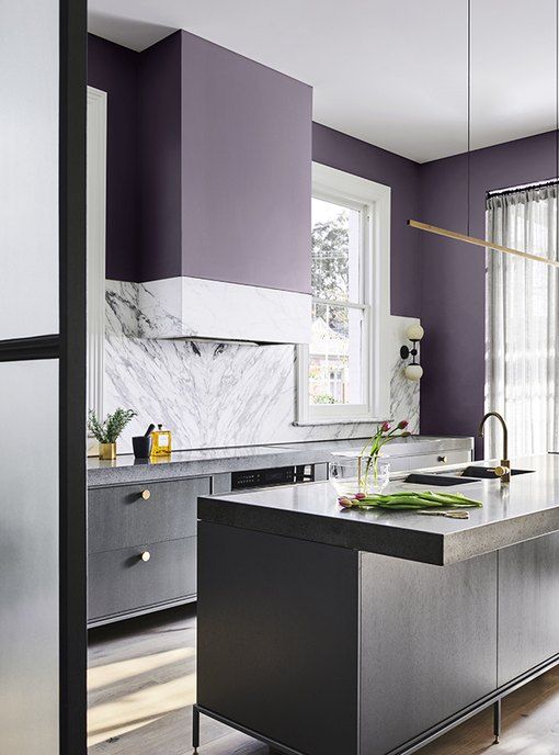 una cucina ultramoderna con armadi grigi, ripiani in pietra bianca e alzatina e pareti viola scuro