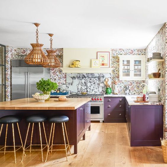 una cucina stravagante con armadi viola, alzatina in marmo e carta da parati con stampa floreale e lampade a sospensione in rattan