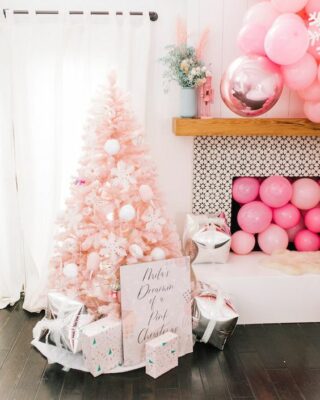 un albero di Natale arrossato con ornamenti bianchi, scatole regalo stampate, palloncini rosa nel camino e sopra
