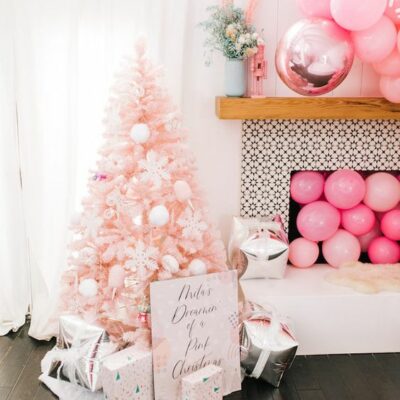 un albero di Natale arrossato con ornamenti bianchi, scatole regalo stampate, palloncini rosa nel camino e sopra