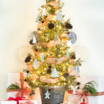 un albero di Natale bello e chic in un cestino, con pigne, mini ornamenti a forma di albero, fiocchi di neve e luci più un cappello a cilindro a stella