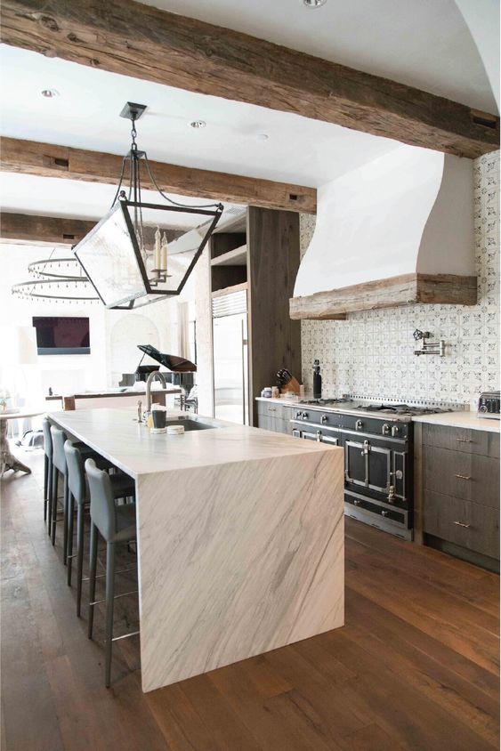 una cucina accattivante con mobili scuri, un'isola della cucina in pietra bianca, travi in ​​legno grezzo e un raffinato lampadario