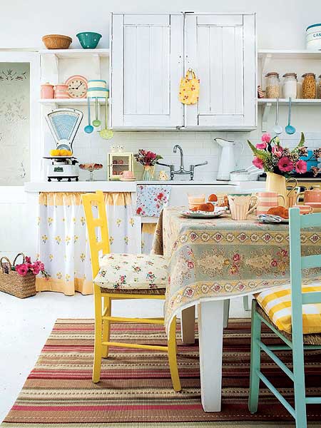 una cucina allegra con mobili bianchi, sedie gialle e blu audaci, tessuti floreali sembra country e molto rilassata