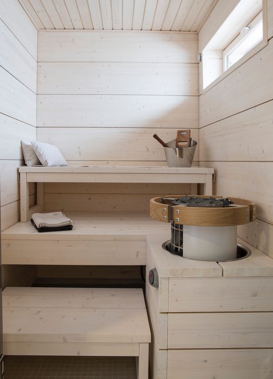un'accogliente sauna in legno imbiancato con un lucernario, tre livelli di panche e alcuni cuscini aromatici