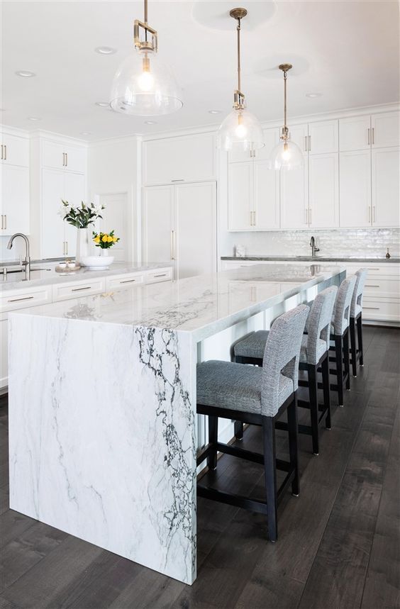 un'elegante cucina bianca con un'isola cucina chic con un piani di lavoro a cascata in marmo bianco che porta il lusso qui