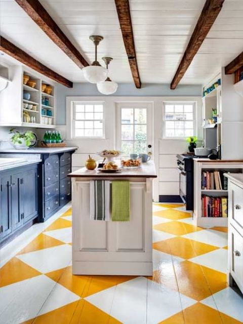 una cucina luminosa con un pavimento geometrico giallo e bianco, armadi blu scuro e travi in ​​legno tinte scure sul soffitto