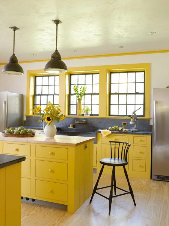 una cucina gialla vintage chic con alzatina e piano di lavoro blu navy e lampade a sospensione nere