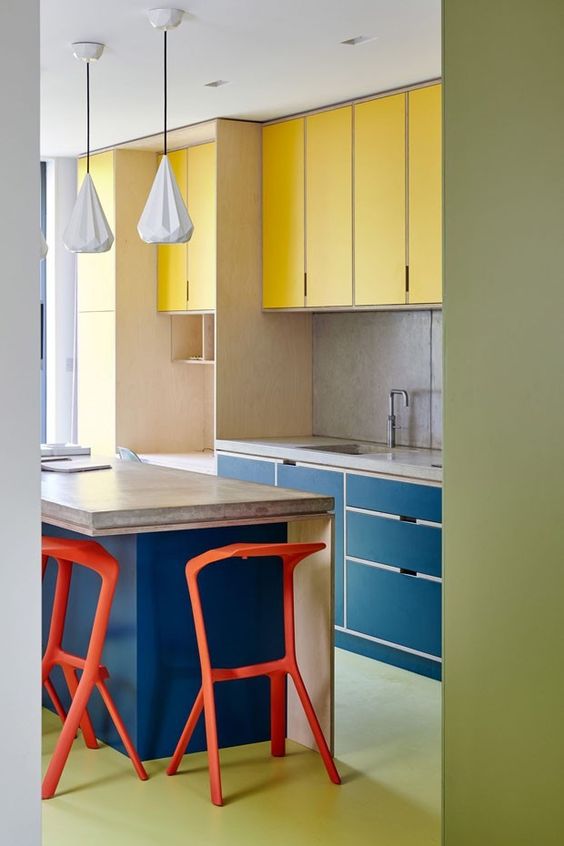 una cucina moderna e colorata in giallo e blu scuro, con un piano di lavoro in pietra, sgabelli rossi e un pavimento verde è molto audace