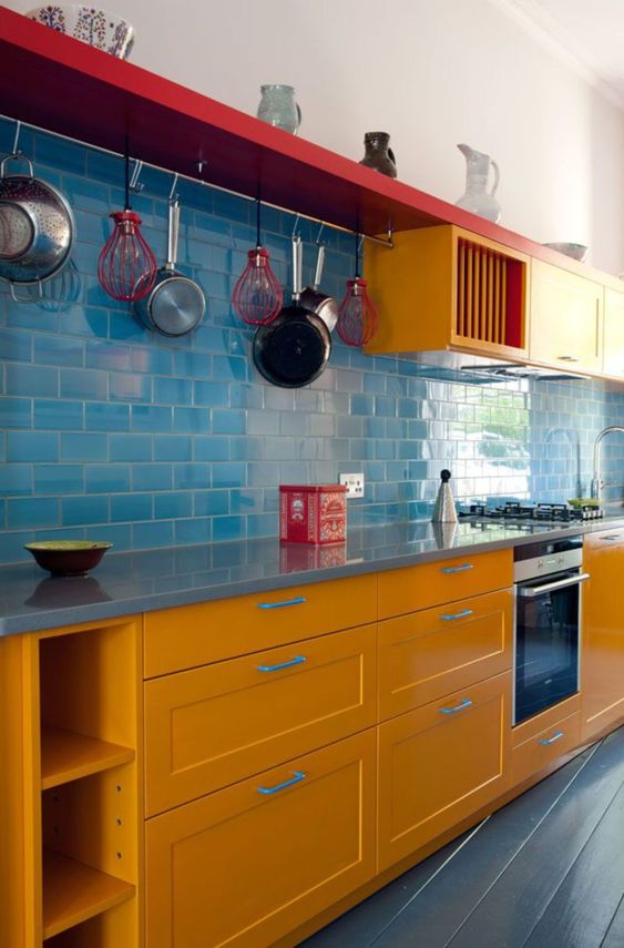 una cucina moderna e colorata con armadi gialli, alzatina piastrellata blu e tocchi di rosso brillante per maggiore audacia