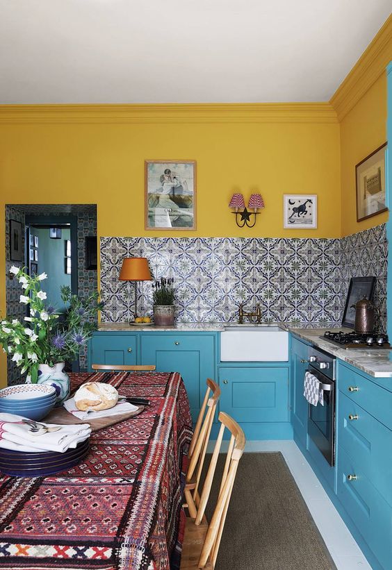 un'accogliente piccola cucina con pareti gialle luminose e piastrelle a mosaico sul backsplash, armadi blu luminosi e applique vintage