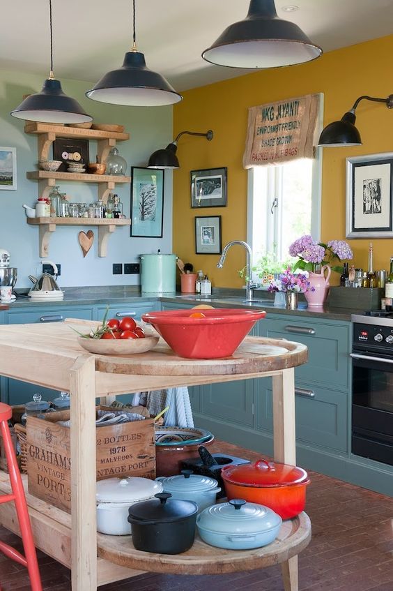 una cucina vintage con armadi blu, un muro senape e azzurro, un'isola da cucina in legno e lampade a sospensione nere