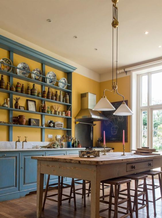 una cucina vintage fatta di crema al burro e con armadi blu e scaffali aperti, con lampade a sospensione vintage e un set da pranzo rustico