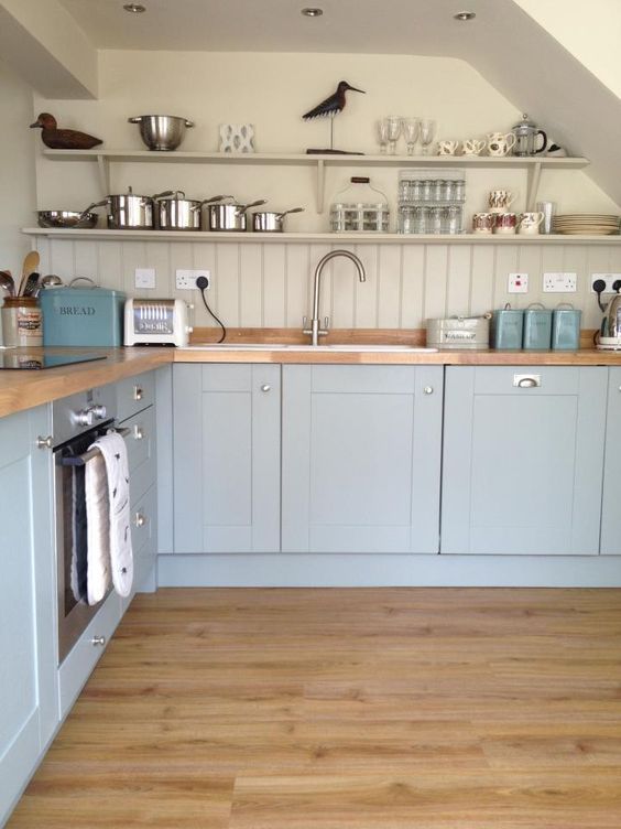 una cucina azzurra con un muro grigio tortora e alzatina in beadboard più controsoffitti in legno per rendere l'aspetto più caldo e morbido