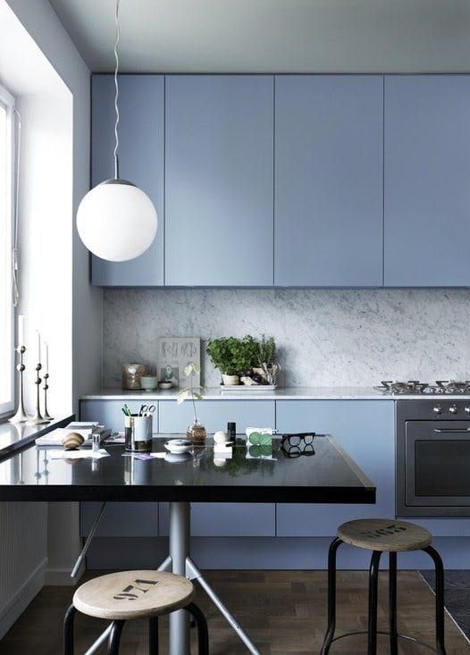 una cucina azzurra minimalista con alzatina in pietra grigia e piani di lavoro rifiniti con sgabelli industriali e un tavolo nero