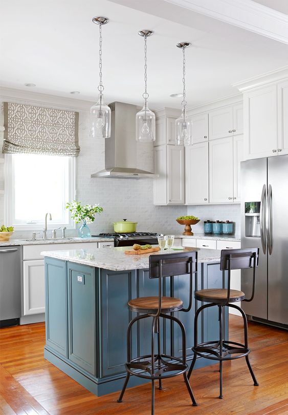 una cucina bianca con un alzatina in piastrelle grigie e un'isola della cucina blu più controsoffitti in pietra bianca è chic