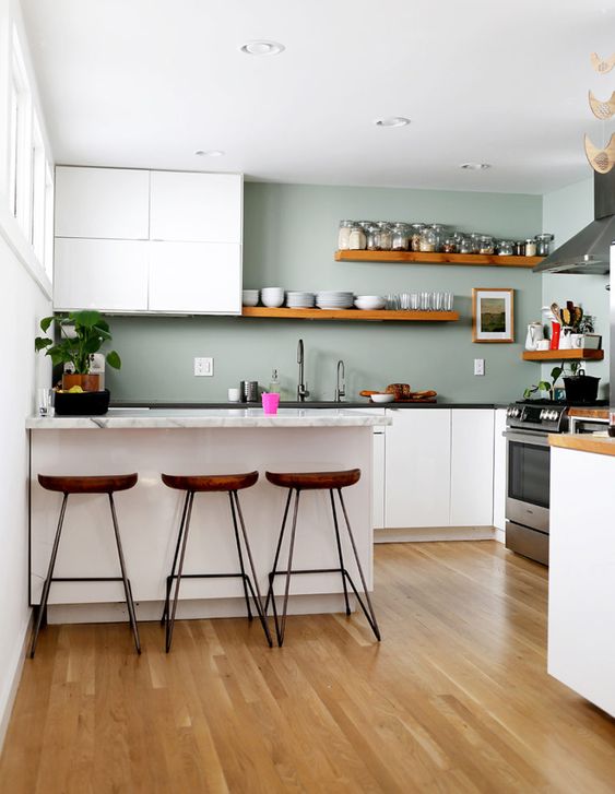 una cucina minimalista con armadi bianchi, pareti verde chiaro, ripiani in pietra e ripiani e sgabelli in legno