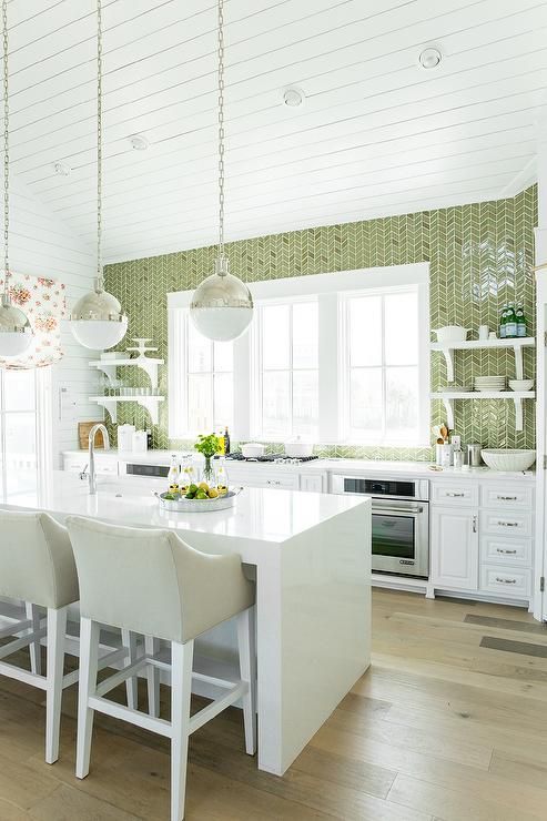 un'accogliente cucina con mobili bianchi, un'isola cucina in pietra bianca, un muro di piastrelle verdi e tocchi di sfumature metalliche