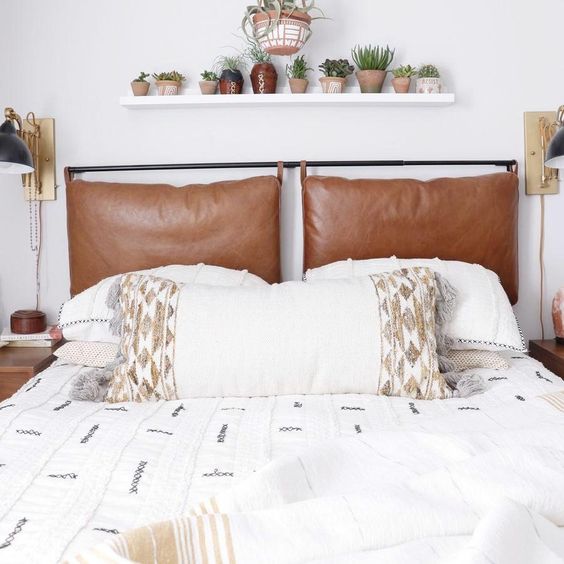 un letto neutro con biancheria da letto ricamata e con nappe e cuscini in pelle marrone come testiera