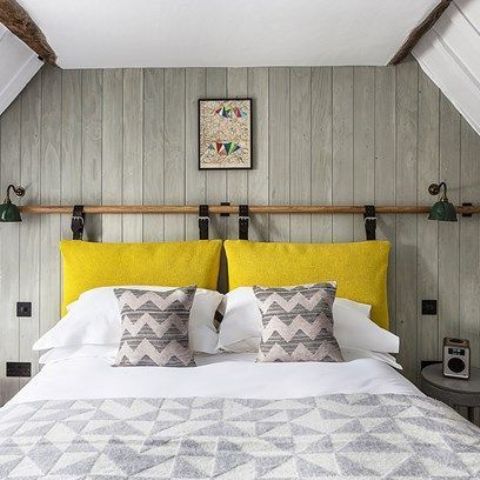 una camera da letto neutra con un sacco di motivi e una testiera del cuscino giallo brillante appesa a cinture di pelle sembra luminosa
