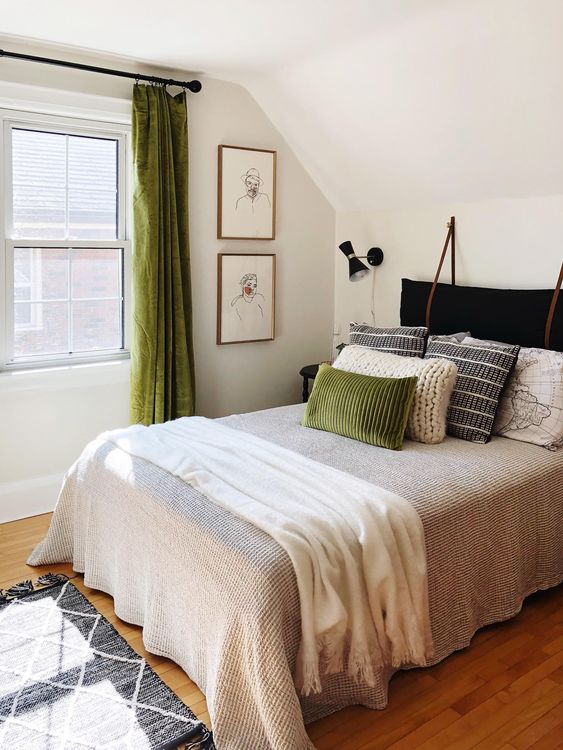 un'accogliente camera da letto con lenzuola verdi, cuscini stampati e lavorati a maglia e una testiera del cuscino in velluto nero