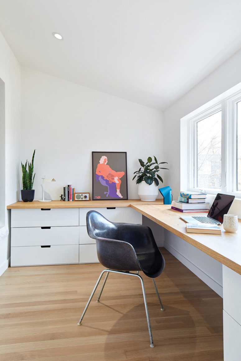Lo spazio di lavoro è fatto con una grande scrivania ad angolo, armadi bianchi, opere d'arte audaci e piante in vaso