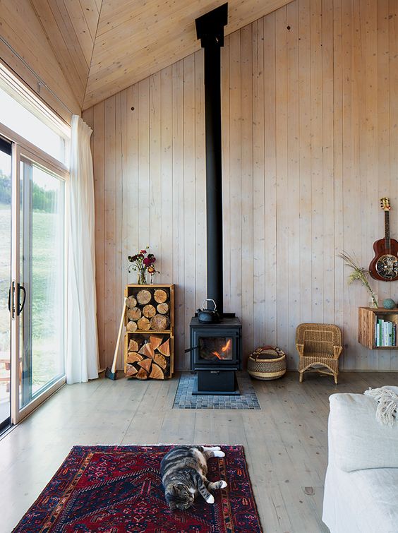 uno spazio cabina completamente rivestito in legno, con una stufa a legna e un po 'di legna da ardere in casse per un'atmosfera accogliente