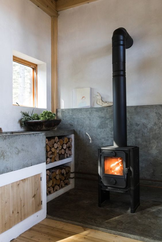 una cucina contemporanea con molto cemento nell'arredamento e una stufa a legna vintage più deposito di legna da ardere