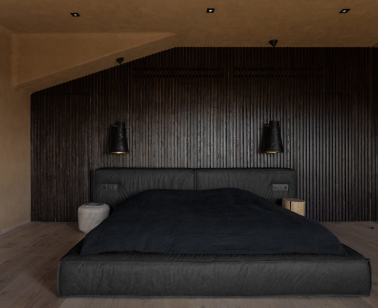 La camera da letto è buia e rilassante, con una parete rivestita in legno, un letto scuro imbottito e applique
