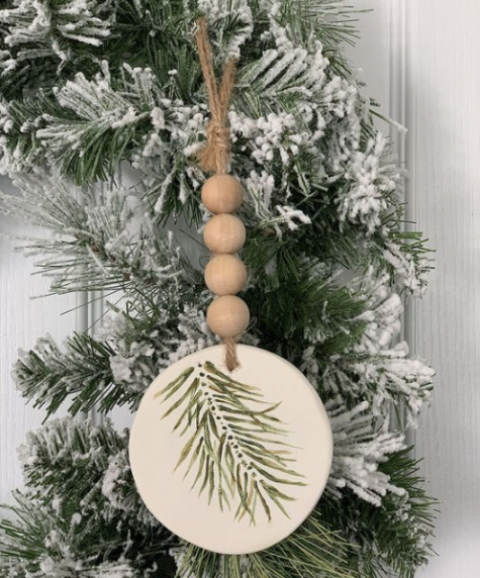un ornamento natalizio rustico di una fetta di legno con sempreverdi dipinti, perline di legno e spago è molto divertente e interessante