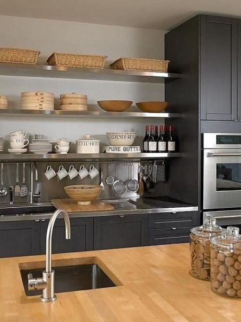 una cucina nera rinfrescata con un alzatina neutra, un piano di lavoro in legno e ripiani, superfici e rubinetti in metallo