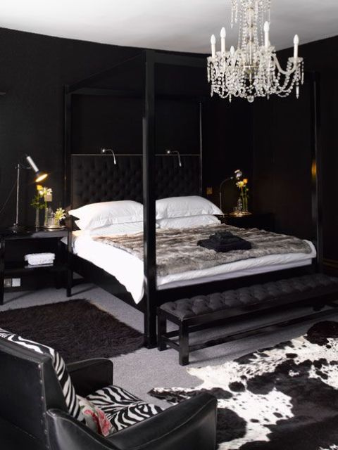 una lussuosa camera da letto con pareti nere, un lampadario di cristallo, stampe animalier e alcune luci sopra il letto