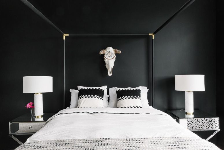 una splendida camera da letto con pareti nere, un letto incorniciato, comodini a specchio e un teschio sul muro
