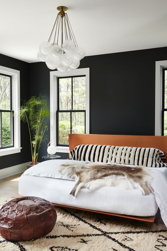 un'elegante camera da letto moderna della metà del secolo con pareti nere, un lampadario creativo, un letto in pelle e finestre bianche