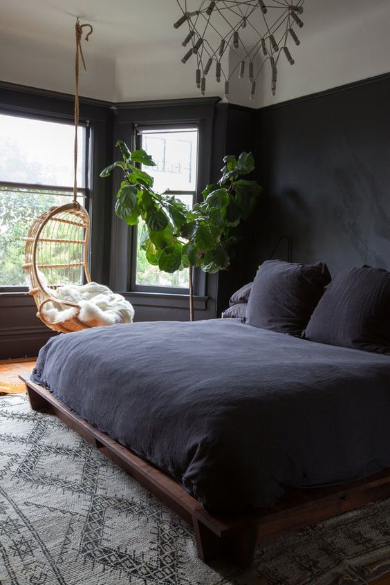un'accogliente camera da letto con pareti nere, piante in vaso, un set da letto nero e una poltrona sospesa