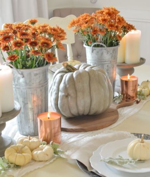 un elegante centrotavola autunnale di zucche bianche e un grande cimelio, fiori arancioni e candele