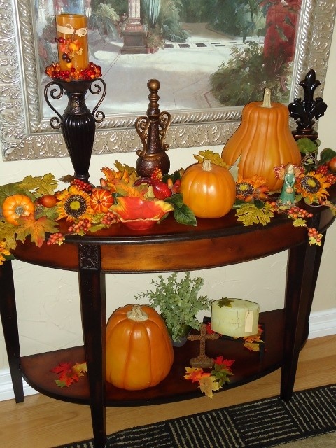 una console in stile con finte zucche, foglie, zucche e bacche più una candela arancione per l'autunno