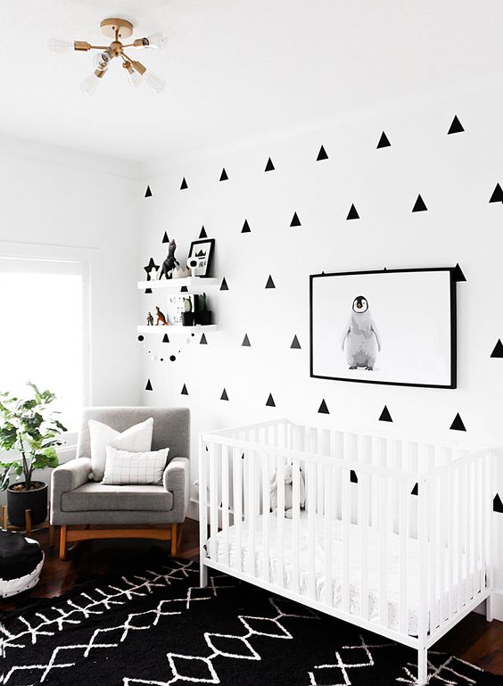 un moderno cameretta in bianco e nero con una parete a motivi geometrici, un tappeto stampato, una culla bianca e un'opera d'arte di un pinguino