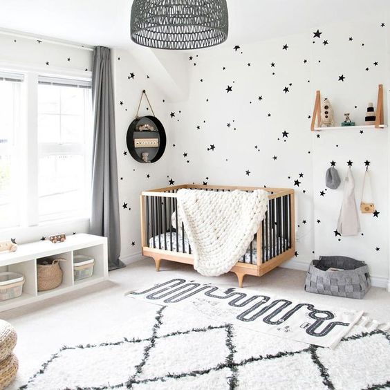 un elegante spazio in bianco e nero con un tappeto stampato, pareti stampate a stelle, una culla contemporanea e un paralume nero