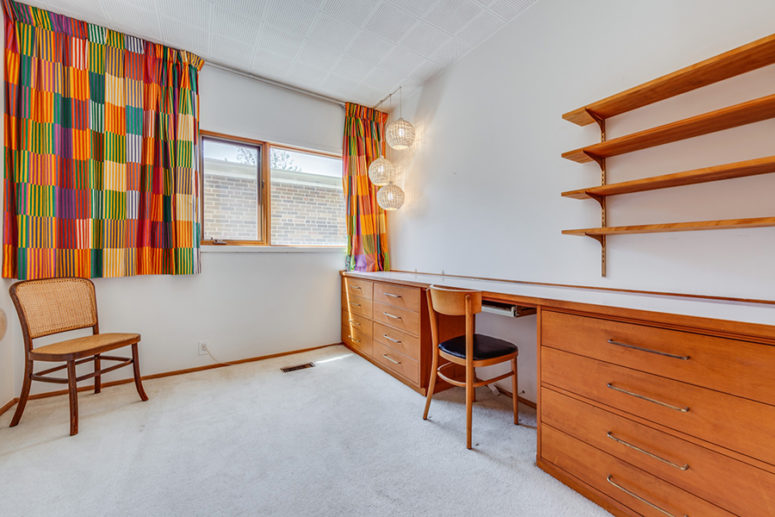 L'home office è dotato di una scrivania in legno di miele di grandi dimensioni, tende colorate, mensole e lampade a sospensione