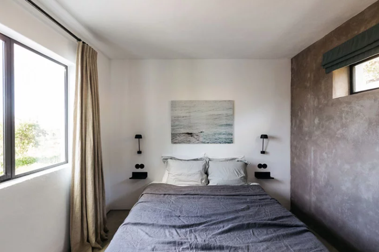 La camera da letto è piccola ma tranquilla, con un muro di cemento, biancheria da letto elegante e un'opera d'arte