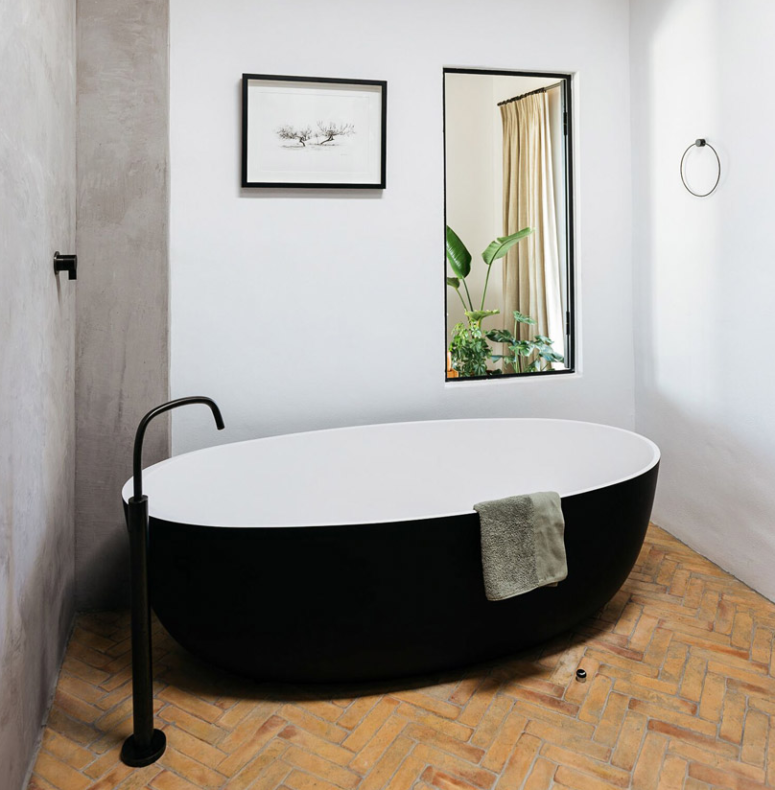 Il bagno è fatto con una vasca bianca e nera, un rubinetto nero e un grande specchio