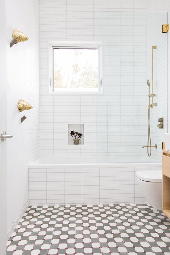 un bagno luminoso con un pavimento a mosaico, piastrelle bianche con ripiani incorporati, una finestra e hardware dorato