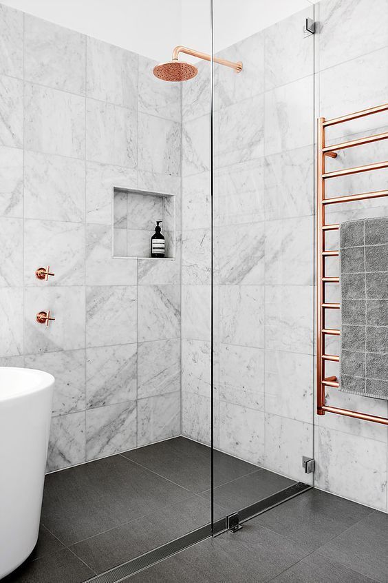 un bagno in piastrelle di marmo con un pavimento scuro, una vasca, una doccia e hardware in rame per un look chic e audace