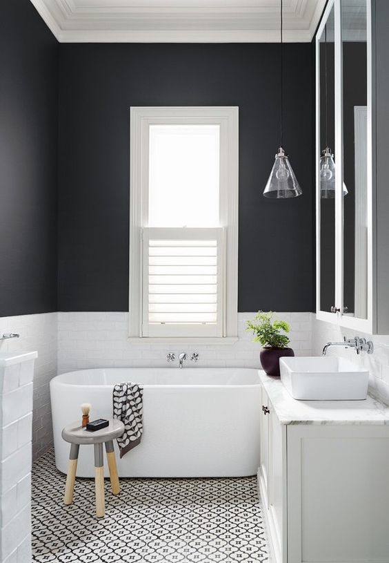 un bagno a contrasto con pareti bianche e nere, un pavimento a mosaico, una vasca ovale, uno sgabello e una lampada a sospensione conica di vetro