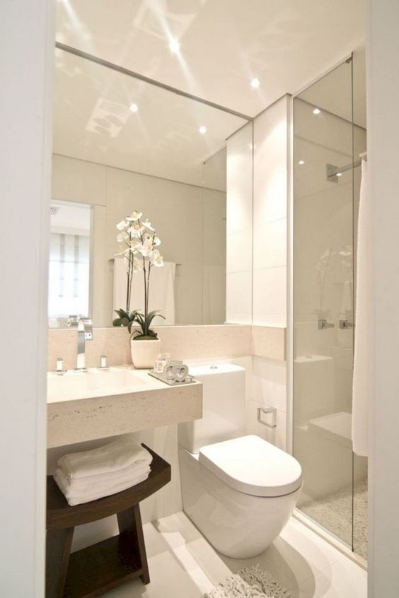 un bagno minimalista neutro con un grande specchio, un lavandino quadrato, uno spazio doccia e uno sgabello in legno tinto scuro