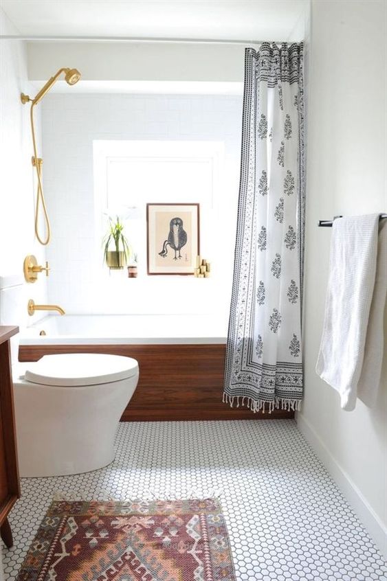 un piccolo bagno moderno con un pavimento in piastrelle penny, una vasca da bagno rivestita in legno, un tappeto, un'opera d'arte e tocchi dorati