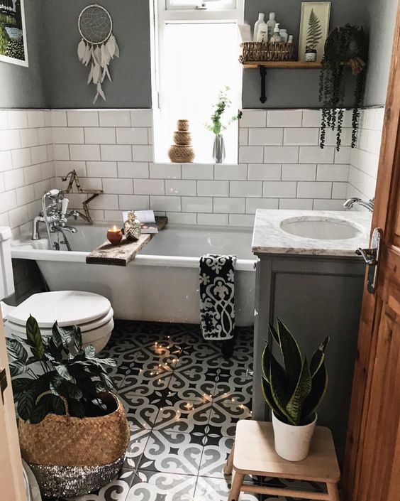 un piccolo bagno boho con pavimento in piastrelle a mosaico, pareti in piastrelle grigie e bianche, una vasca, vegetazione in vaso e cestini per la conservazione