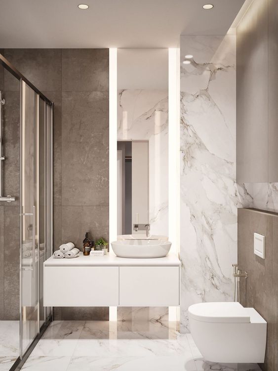 un piccolo bagno minimalista con piastrelle in marmo, uno spazio doccia, un lavabo sospeso e uno specchio alto con luci