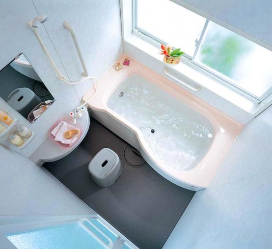 un grazioso piccolo bagno fatto con una vasca rosa e una doccia, un lavabo sospeso con un lavandino, un tavolino e uno specchio